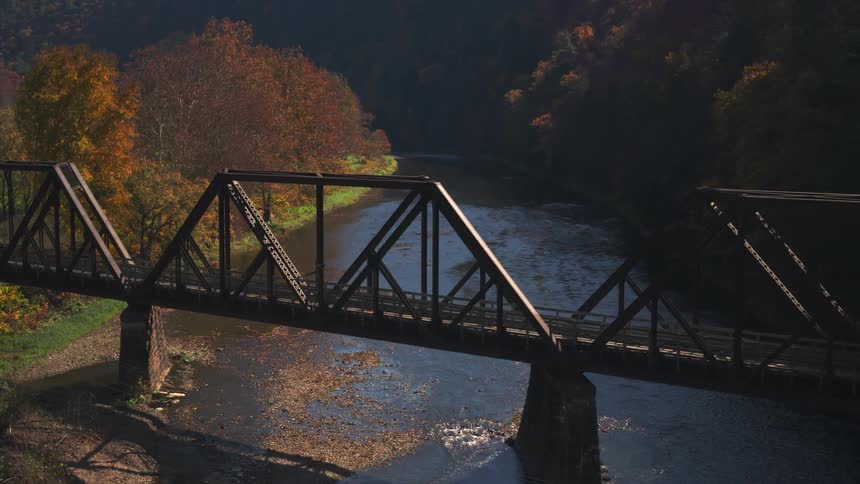 Aerial view of a steel truss bridge over a river with autumncolored trees lining the riverbank