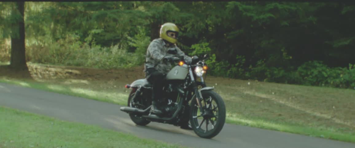 A person wearing a yellow helmet rides a motorcycle on a tree lined road