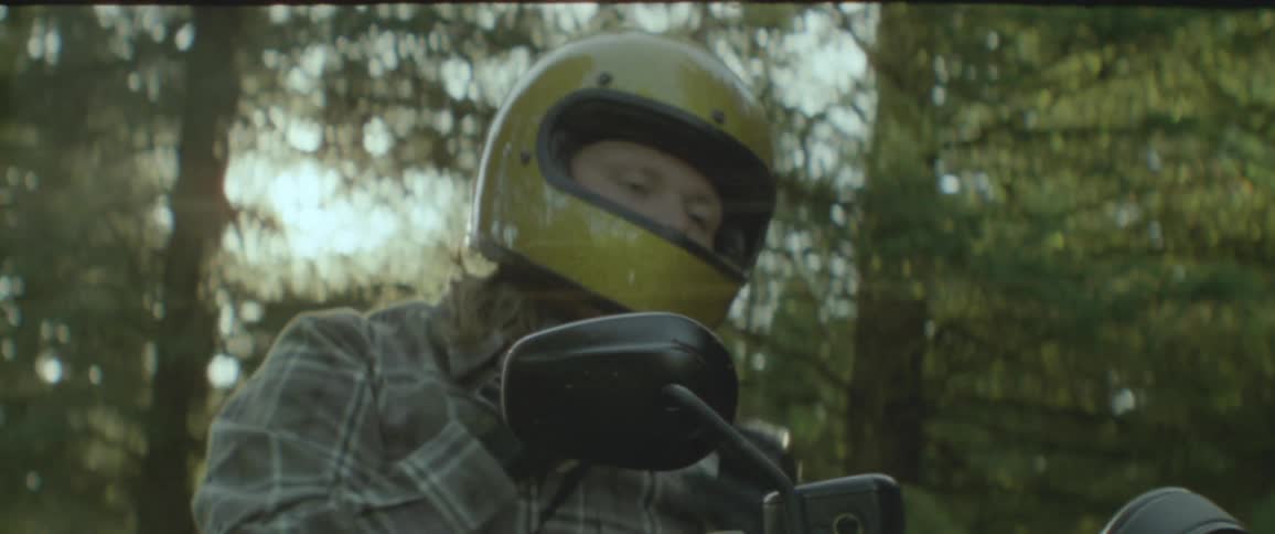 A motorcycle rider wearing a yellow helmet takes off their sunglasses and hangs them on their shirt