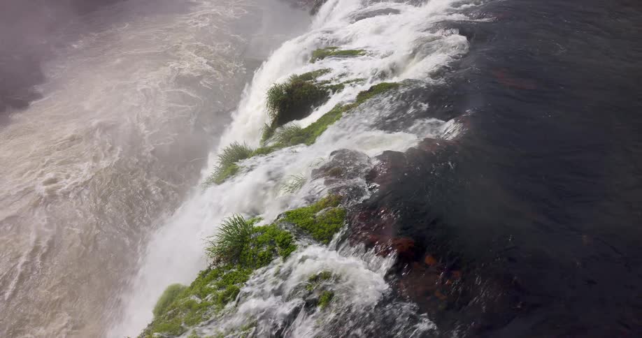 White water rushes over the edge revealing mossy rocks beneath the roaring cascade