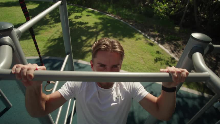 A man is exercising at an outdoor gym during the summer