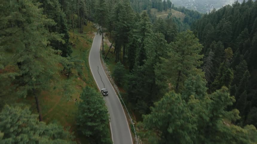 A car driving on a pile of asphalt where there is a forest of trees on the sides seen from above