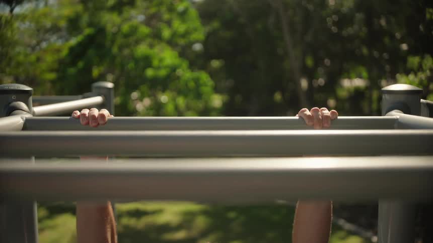 Man performs chin ups on the monkey bars at the park on a summer day