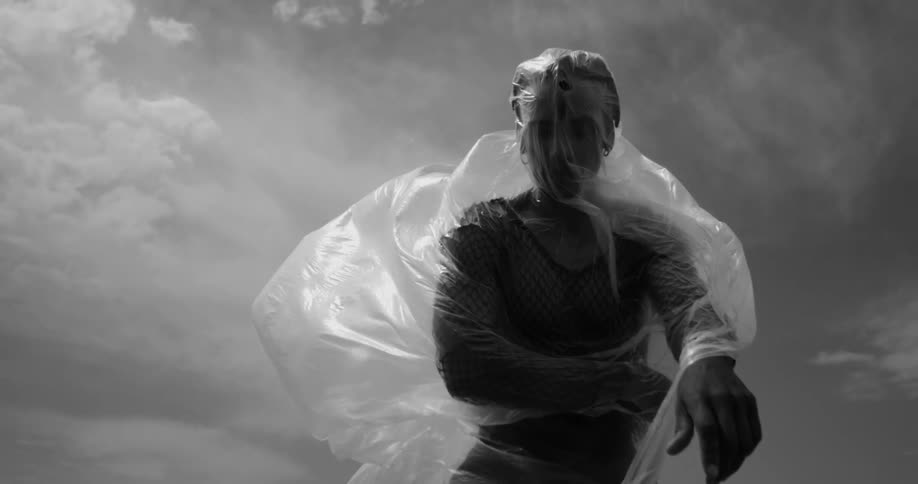 A person is wrapped in plastic with the plastic billowing out behind them set against a cloudy sky