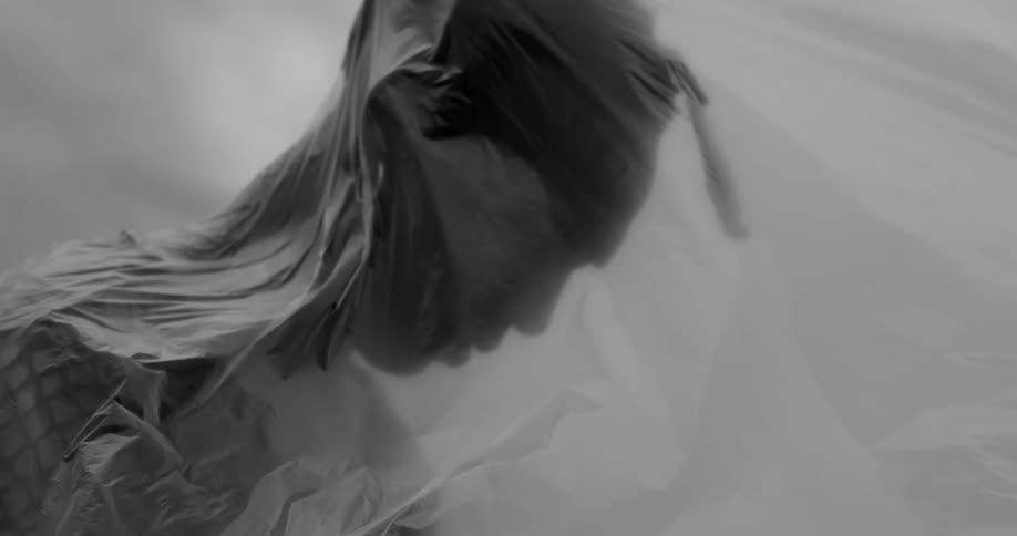 A person is wrapped in plastic with the plastic billowing out around them set against a cloudy sky