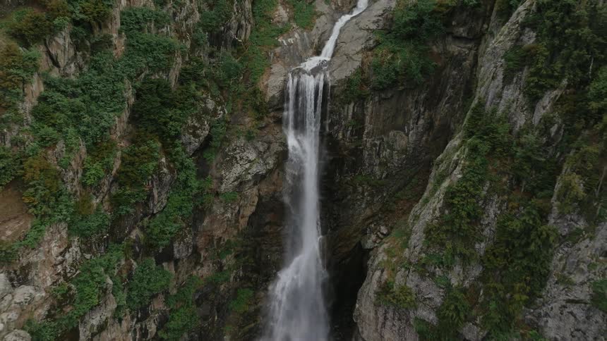 Flying upwards from a close view of a waterfall cascading down a mountainside