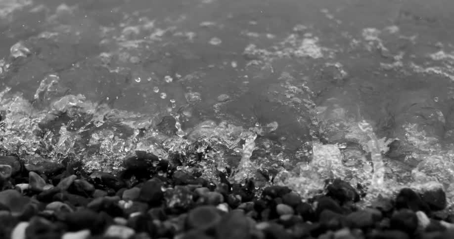 S waves gently crashing onto a rocky shoreline with water droplets suspended mid splash