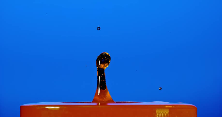 A drop of water falling on an orange surface and making an upward splash