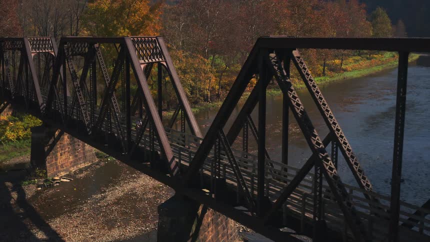 A cyclist crosses a steel truss bridge over a river with autumncolored trees lining the riverbank