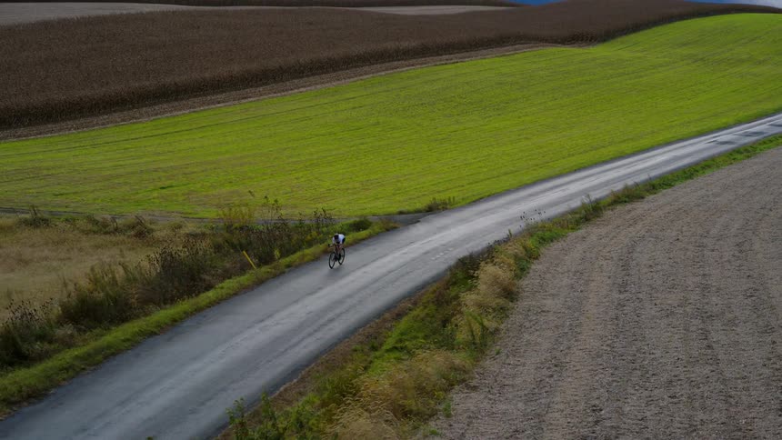 Cyclist rides alone on a country road surrounded by fields
