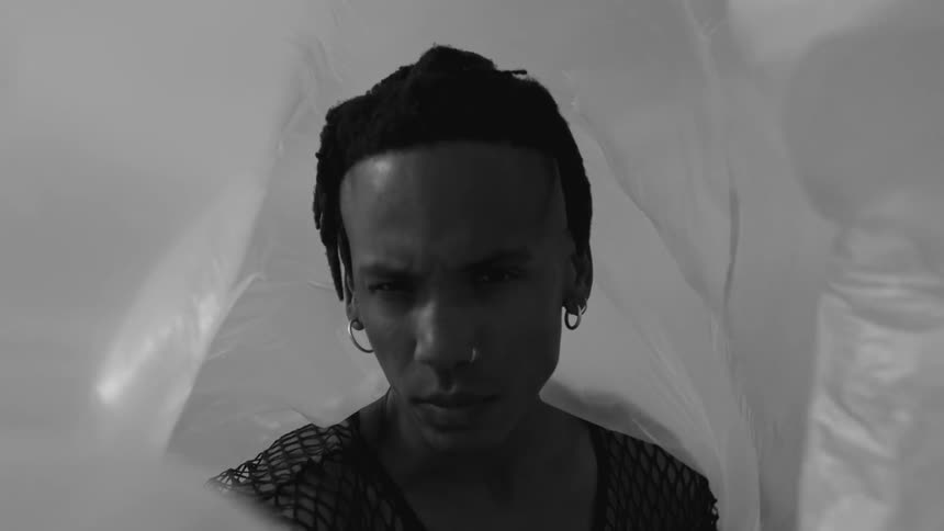 Man wearing differently sized hoop earrings stands surrounded by rippling plastic