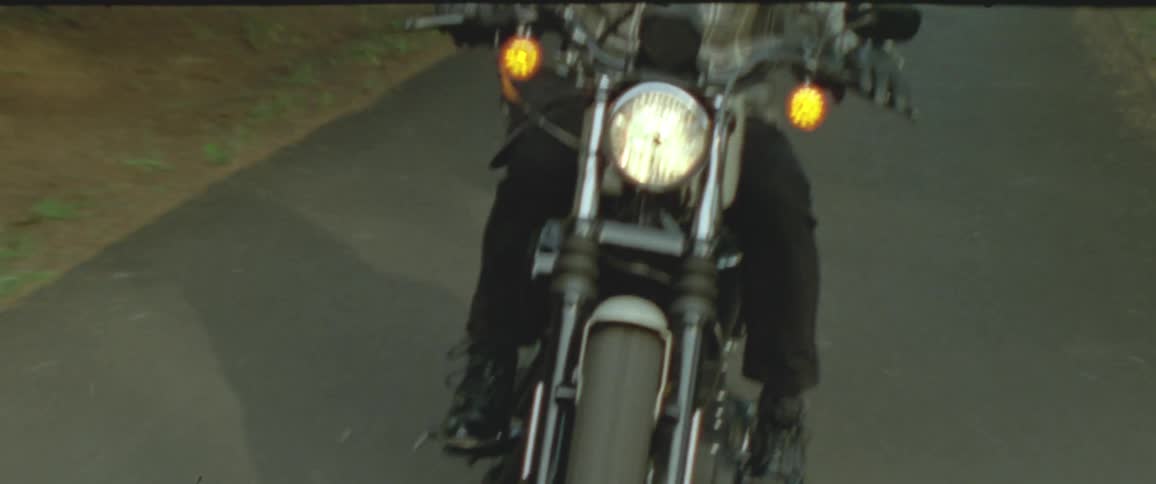 Motorcycle rider drives down a road with trees and grass on each side of it