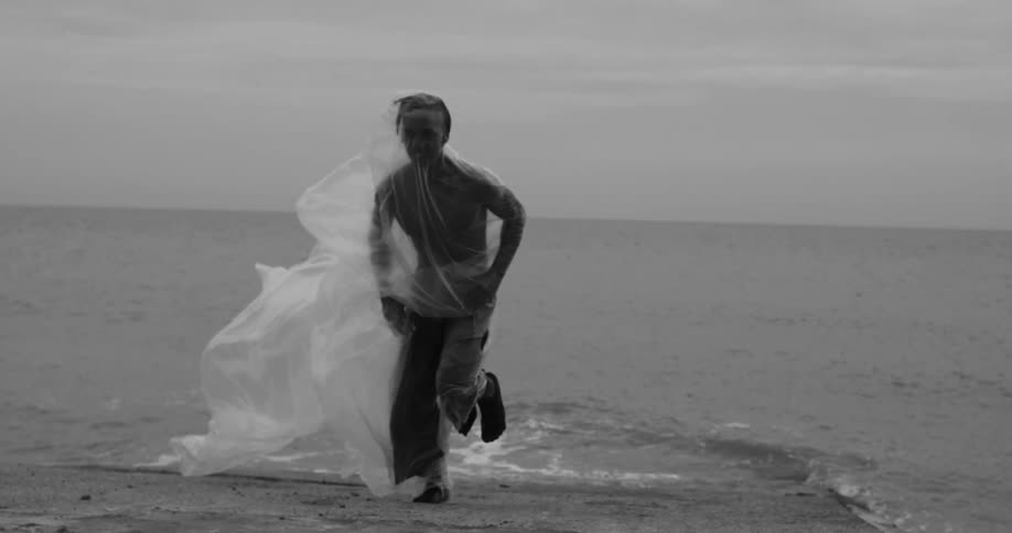 A man runs in extremely slow motion out of the ocean onto the shore