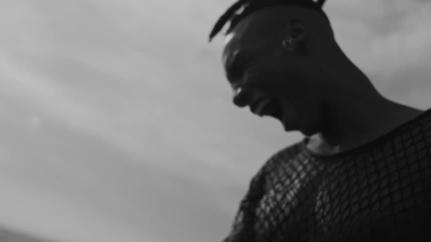 A person wearing a mesh shirt and earrings looks down and begins to yell