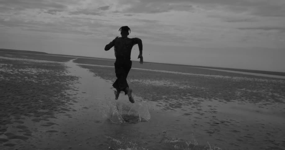 A person runs barefoot through shallow water on a beach splashing as they move