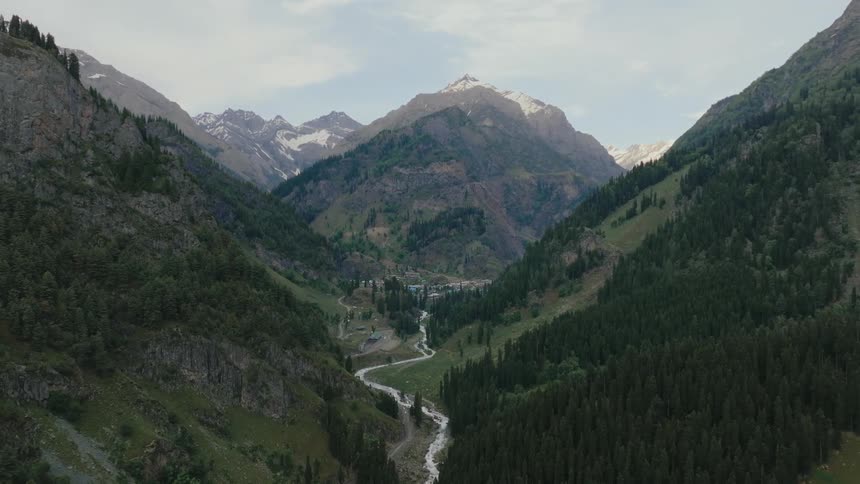 A winding river flows through a lush mountainous valley beneath a cloudy sky