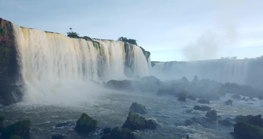 A powerful waterfall plunges from tall cliffs sending clouds of mist into the air as water flows around scattered rocks