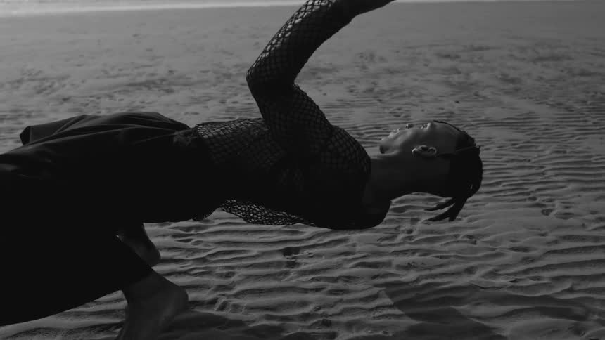 A man in a netted long sleeve top collapsing backward onto beach sand