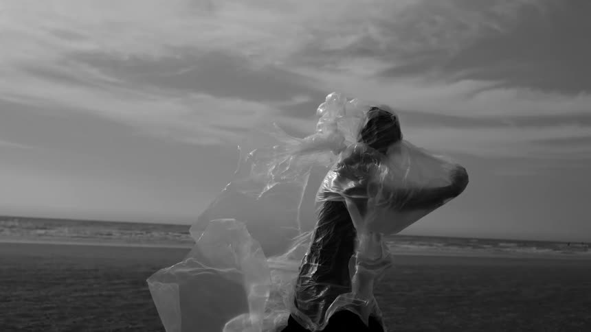 Person wrapped in a clear plastic bag walking on the sand at the beach