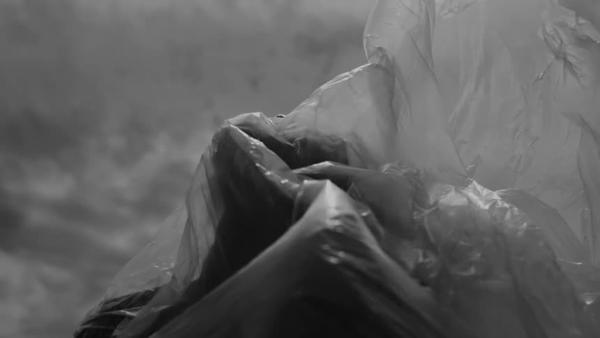 A person is wrapped in plastic with the plastic billowing out behind them set against a cloudy sky