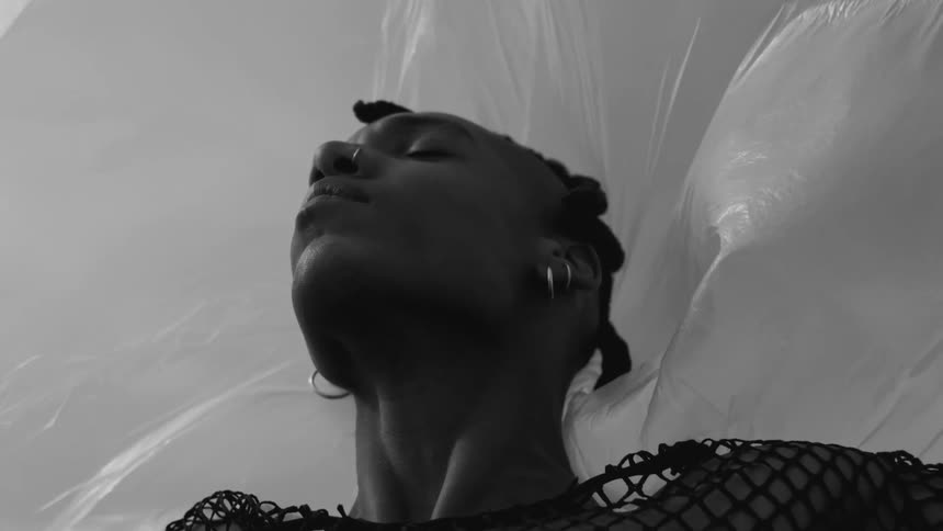 The face of a young woman in person wearing earrings with her eyes closed and with a white sheet in the background moving