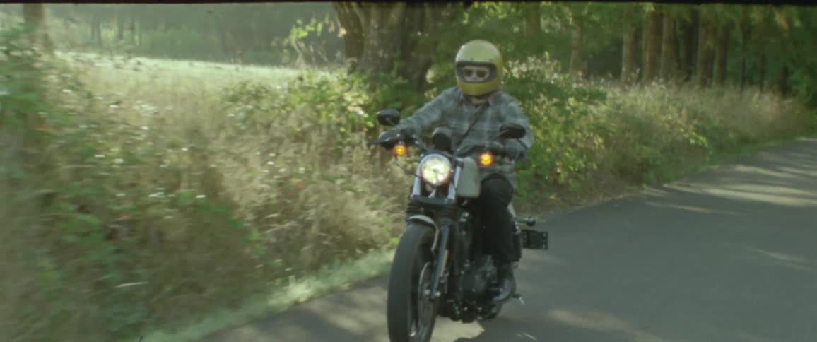 A person wearing a helmet rides a motorcycle on a paved road in the countryside on a sunny morning