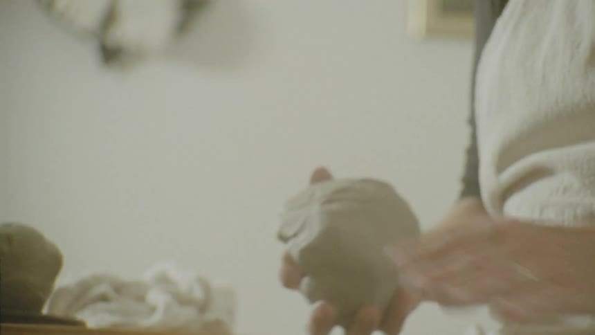 Two hands are shaping a piece of clay on a pottery wheel