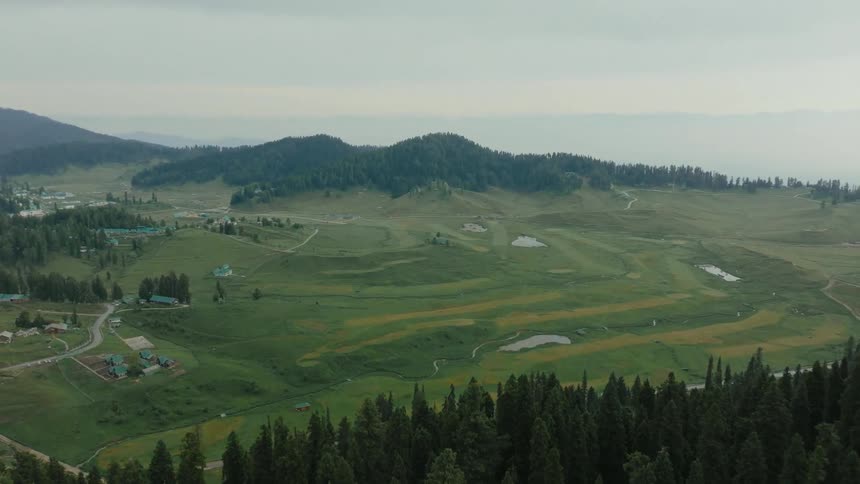 Aerial view of a vast field with houses and forest in the background