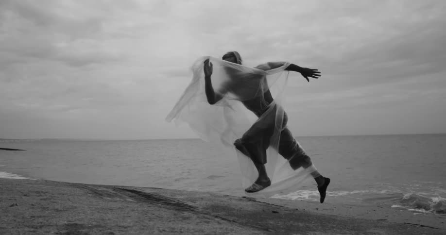 A person is wrapped in plastic with the plastic billowing out behind them running on a beach
