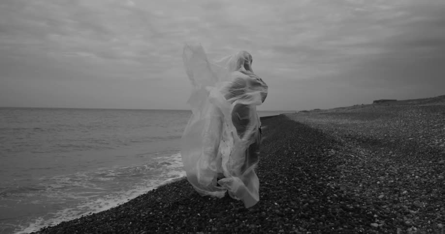 A person is standing on the beach covered with plastic as the wind blows