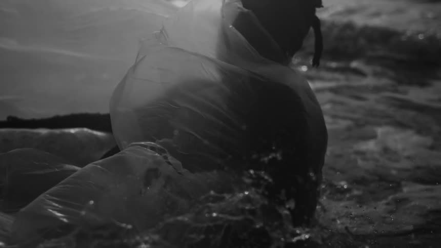 A man covered in a plastic sheet falls into the ocean