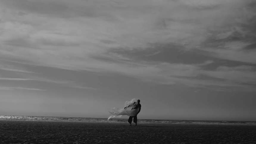Silhouette of a person holding a clear plastic bag on the sand at the beach
