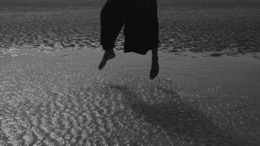 Legs of a person in midair falling towards shallow water with sand