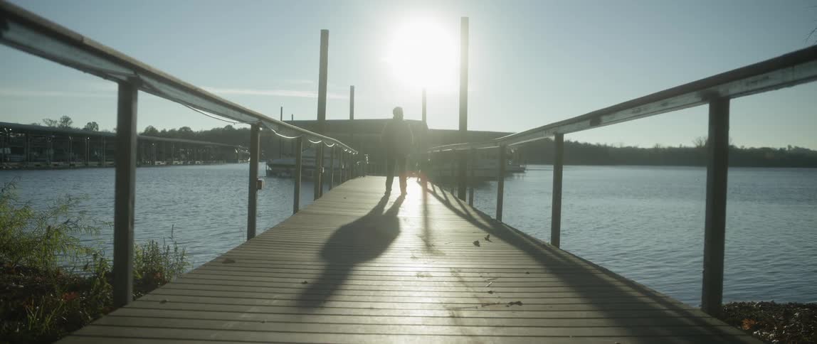 A person stands on a pier with the sun shining overhead