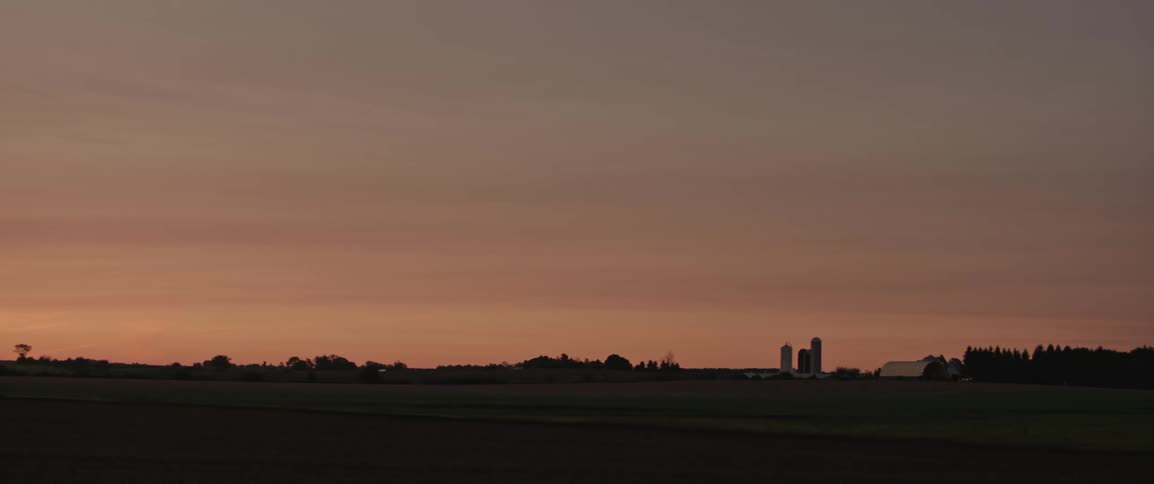 Silhouettes of barns and grain silos as the sun rises over the countryside