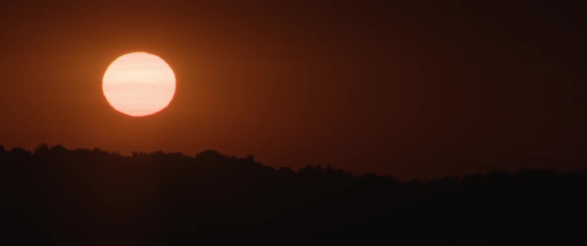 Silhouette of a mountain with the sunrise on the horizon and a reddish sky