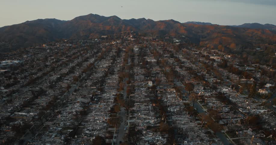Aerial view of a devastated neighborhood with charred ruins and mountains in the background