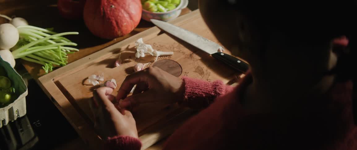 A person is peeling garlic on a wooden cutting board in her sunny kitchen