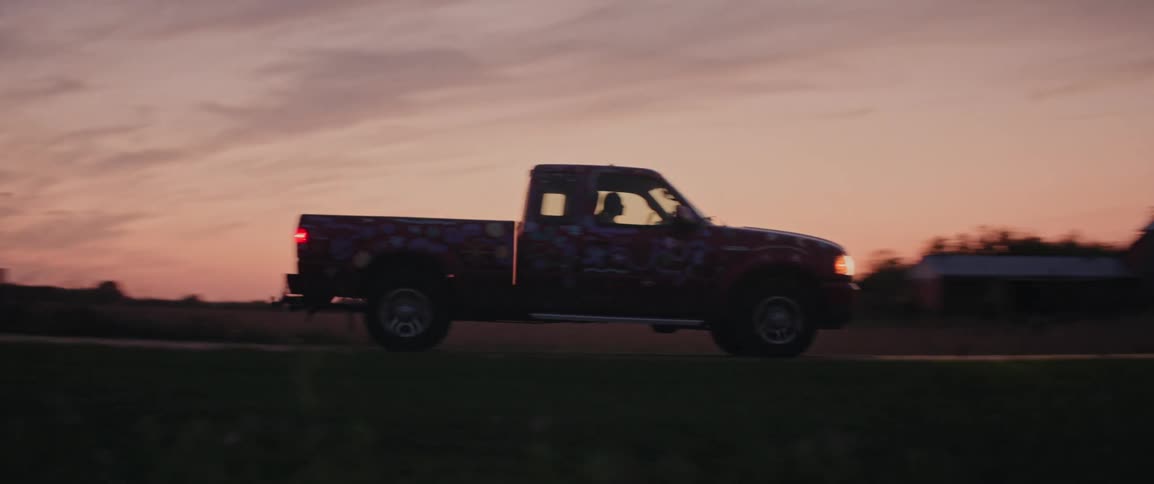 Lone vehicles traveling along a paved road surrounded by agricultural fields on a red sky sunrise