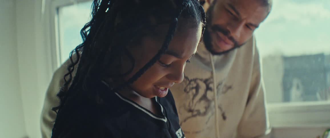 A father helps his daughter with a task in a sunlit room