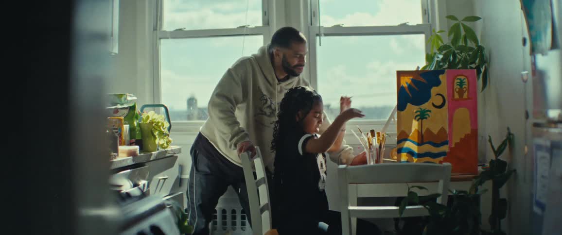 A father helps his daughter while painting picture in a sunlit room