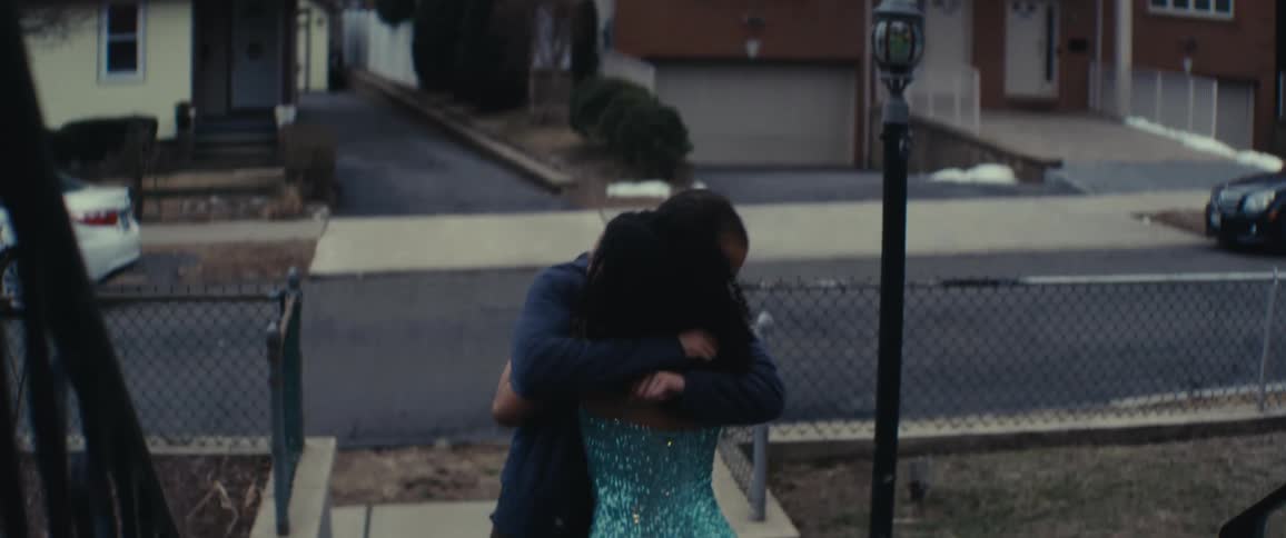 A father looks surprised when he sees his teenage daughter in a shiny blue dress and he hugs her on the front porch