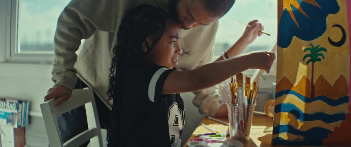 Girl painting a picture and getting a kiss on the forehead from her father