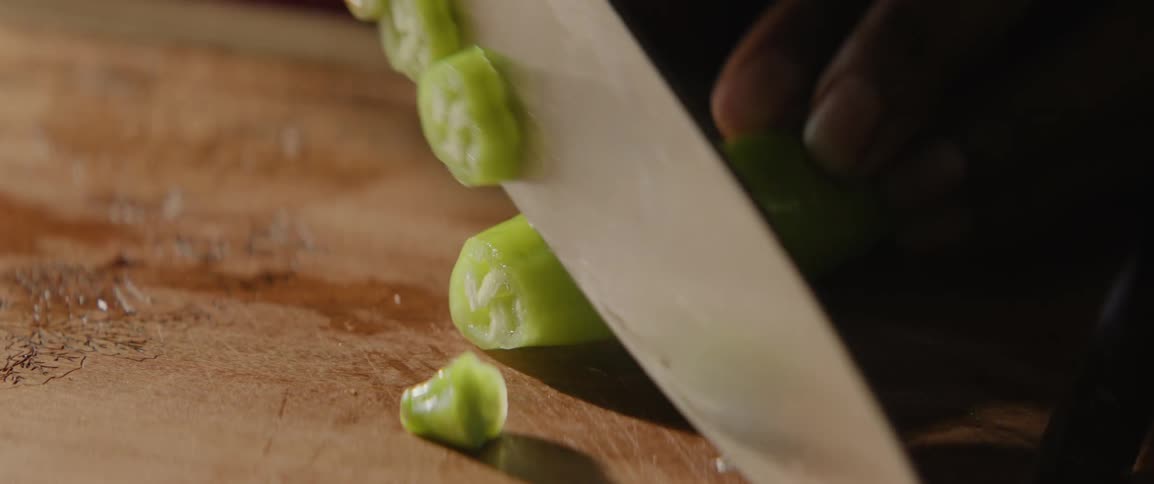 A person is cutting up a pepper with a large knife