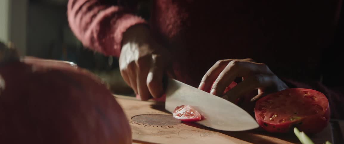 Slicing a large tomato on a wood cutting board with a sharp chefs knife
