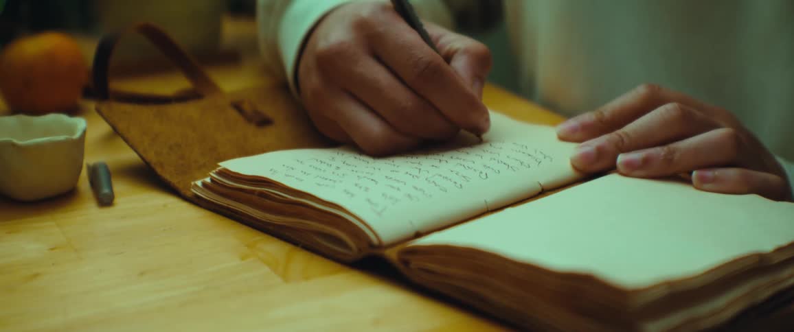 Person sitting at a table and writing in their journal