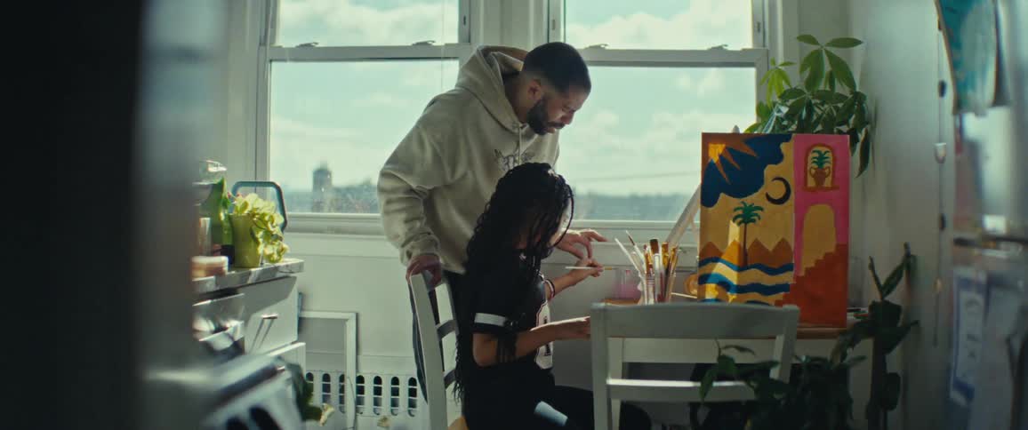 A father is watching his daughter paint by the window