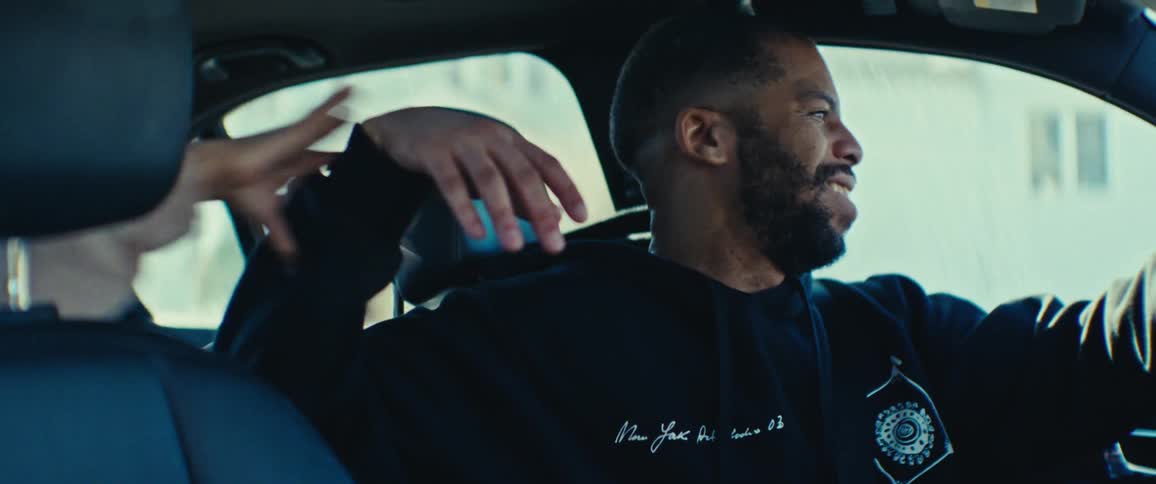Closeup of a man sitting in the front seat of a car playing and joking with someone in the back seat