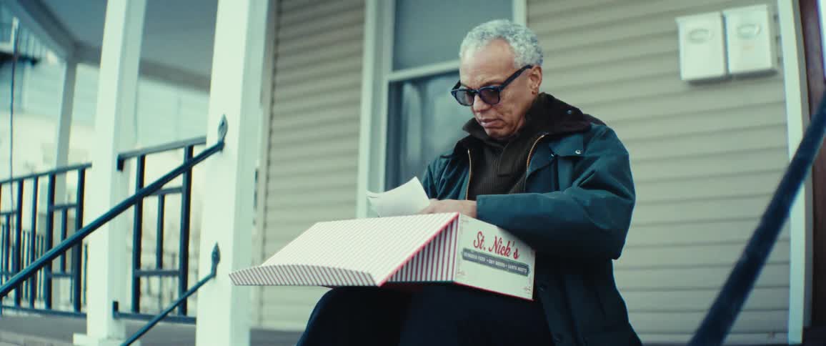 An individual sits on the steps of a porch opening a striped and examining its contents