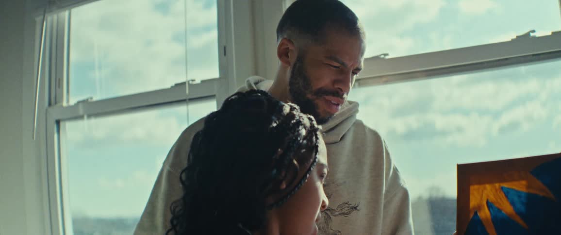 A father helps his daughter while painting picture in a sunlit room